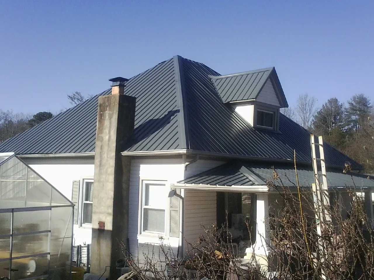 Dark blue standing seam metal roof on a white farmhouse with dormer — Slate & Tile Roof Repair by Roofing Brothers in Montvale