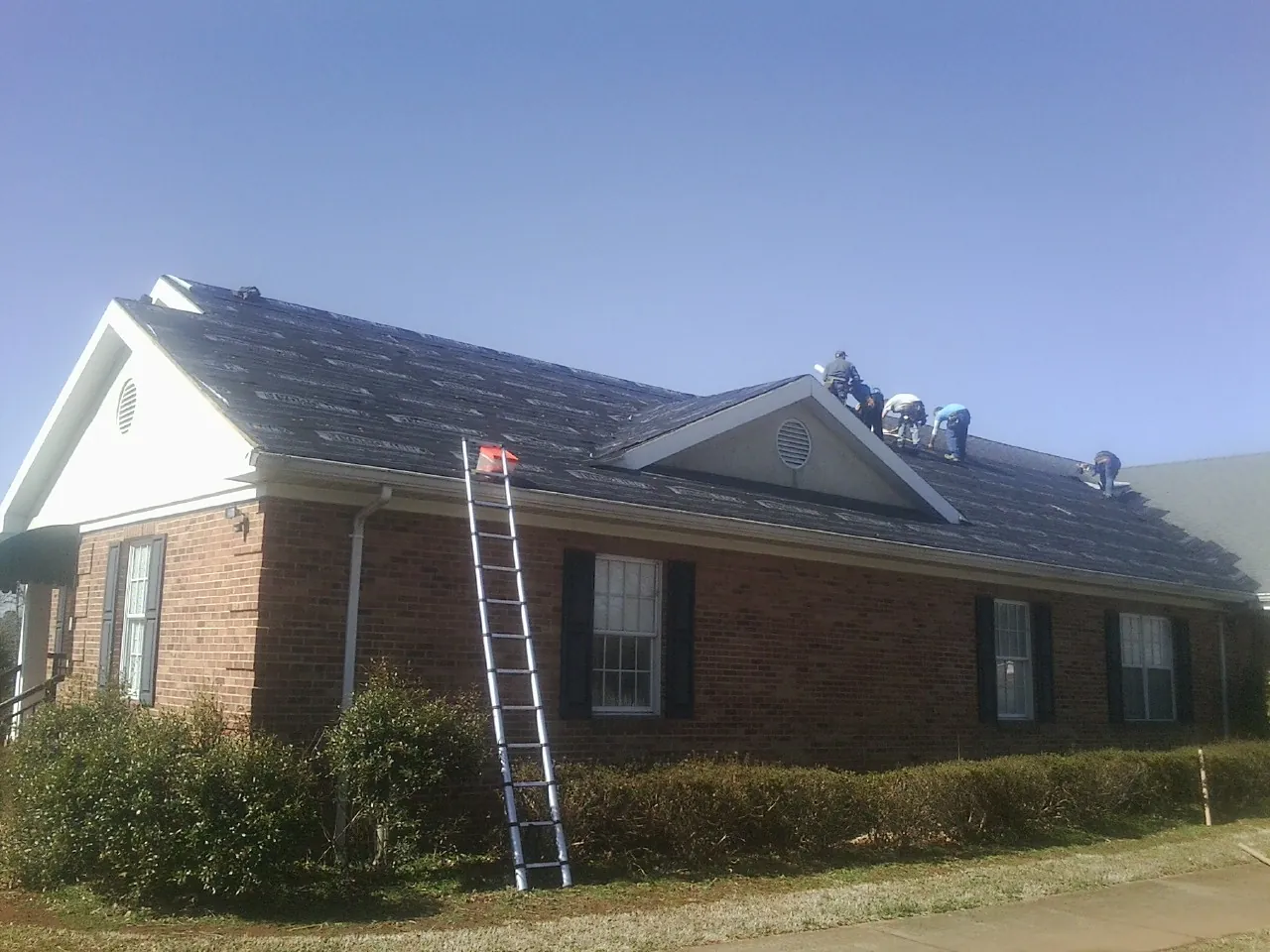 Crew tearing shingles off a brick ranch roof with a ladder set — Emergency Roof Repair work by our crew in Montvale