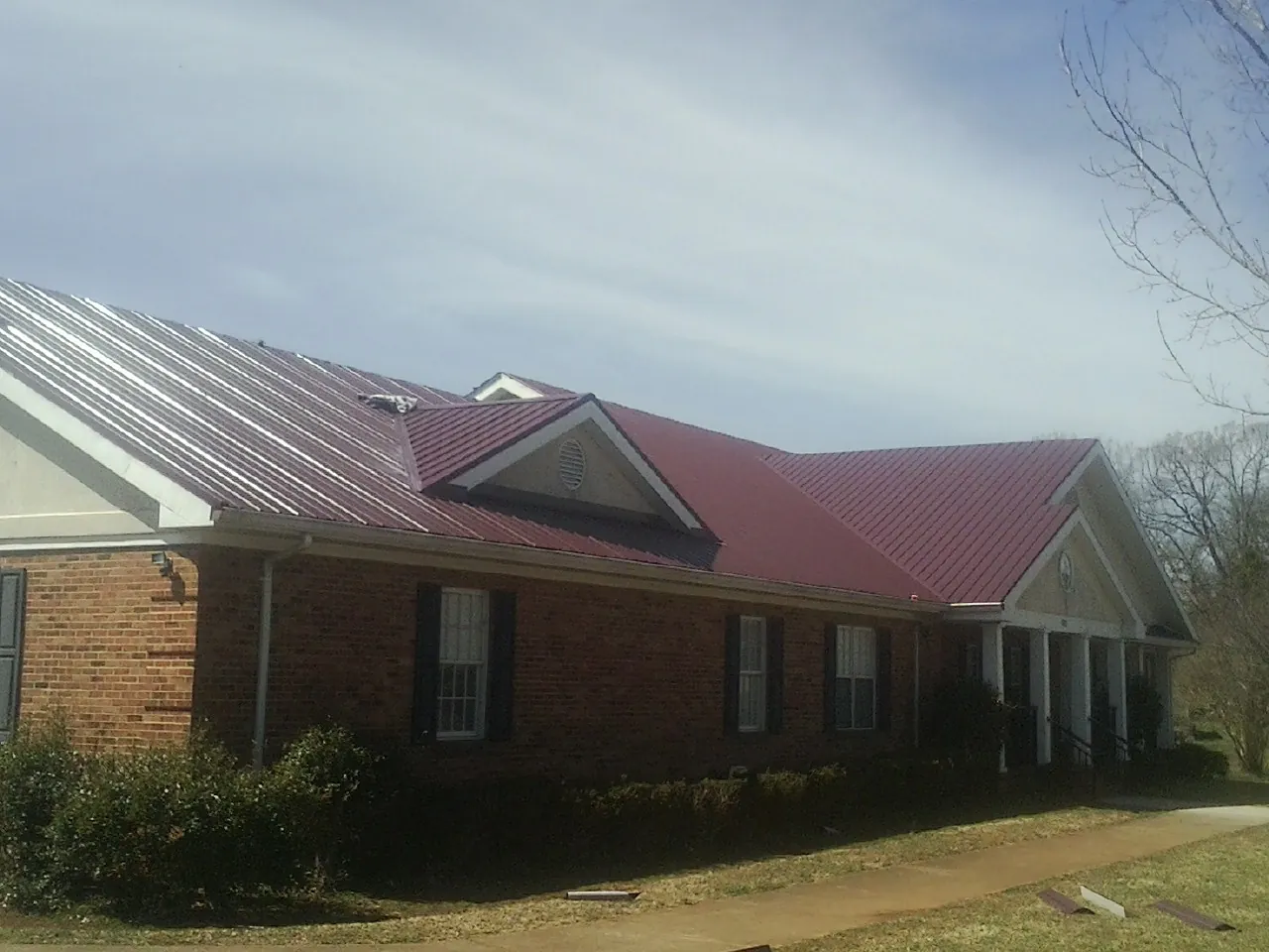 Red metal roof with gabled entries on a long brick building, from a Hail Damage Roof Repair job in Montvale