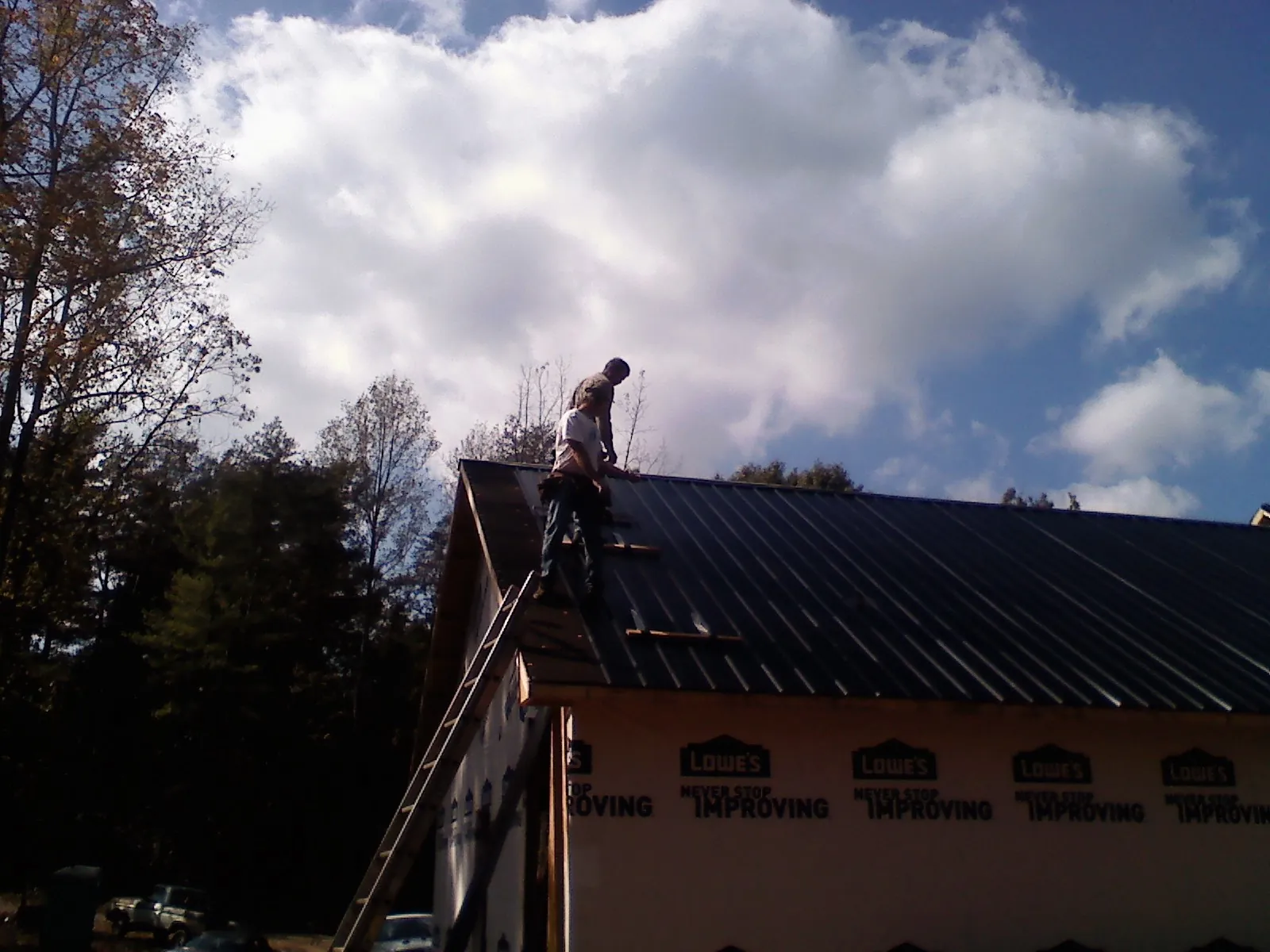 Roofer fastening dark metal panels high against a cloudy sky, from a Roof Inspection job in Montvale
